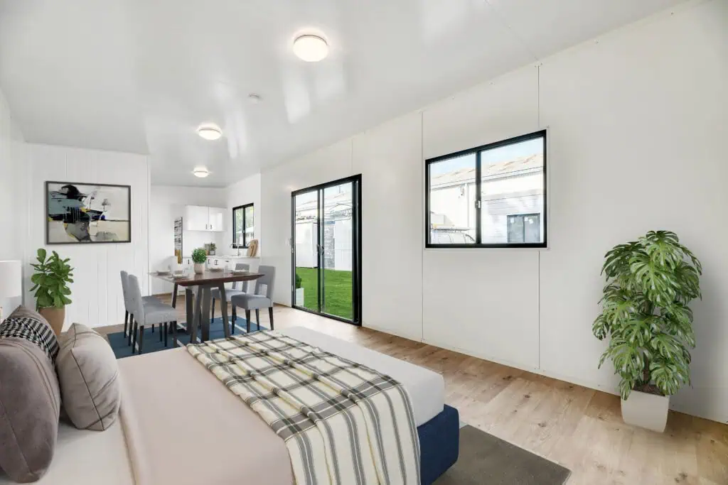 Relocatable building interior showing a living space with white walls, a bed in the foreground, and a small kitchenette in the background