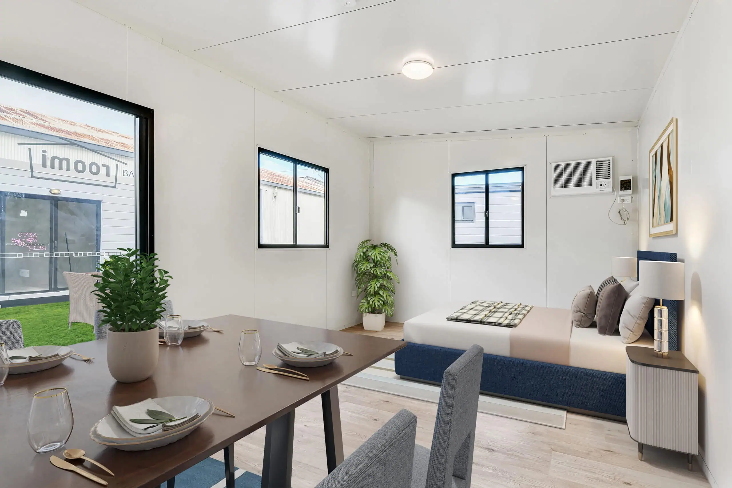 Stylish studio-style modular living unit with a queen bed, dining set, and plants, showcasing a finished kit home interior